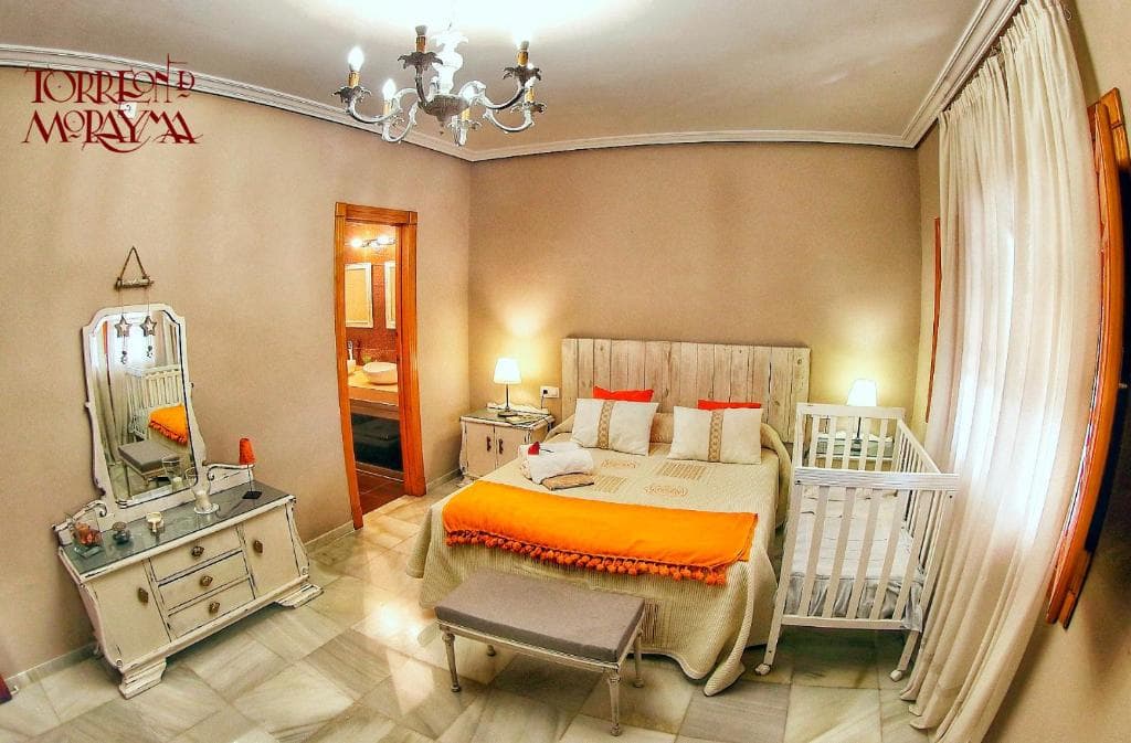 Dormitorio con lámpara de araña, tocador antiguo y cuna junto a la cama